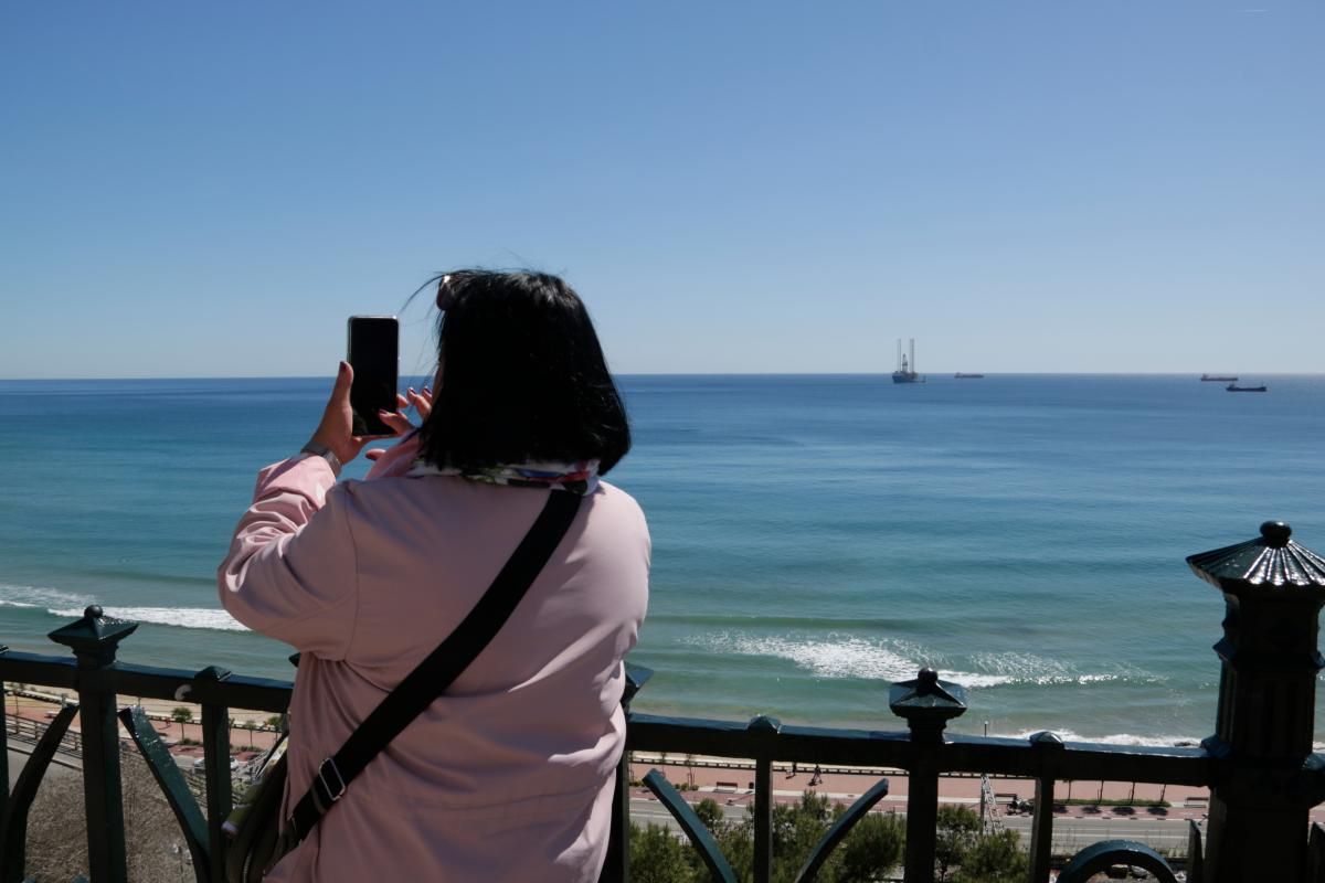 Una dona fotografia la mar a Tarragona, aliena a l'arribada de la plataforma d'operacions que segellarà els pous submarins del projecte Castor