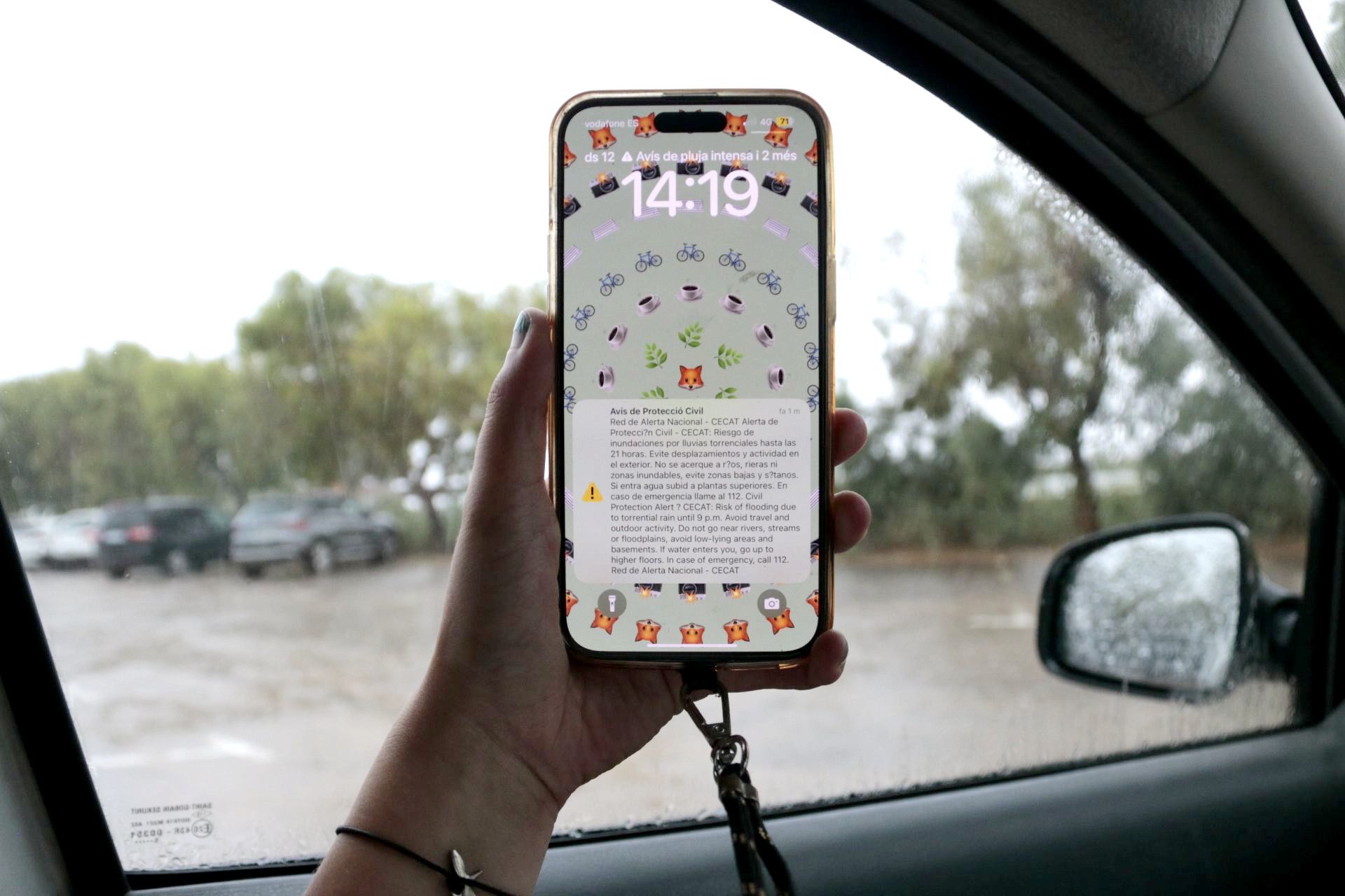 Un telèfon mòbil, amb l'alerta de Protecció Civil, i un carrer ple d'aigua de pluja al fons, a Amposta Un telèfon mòbil, amb l'alerta de Protecció Civil, i un carrer ple d'aigua de pluja al fons, a Amposta