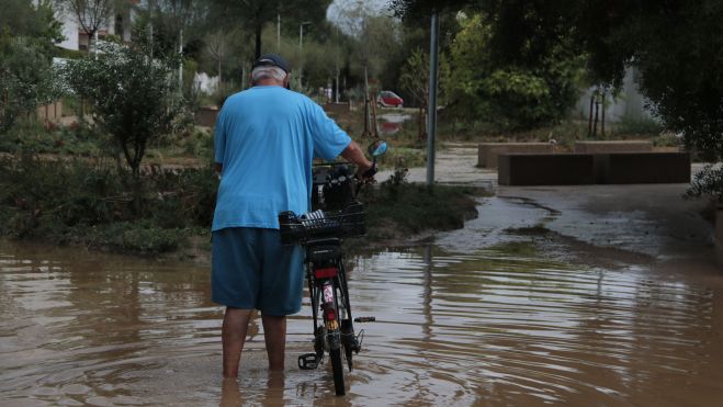 Un home travessa una zona inundada amb la seva bicicleta